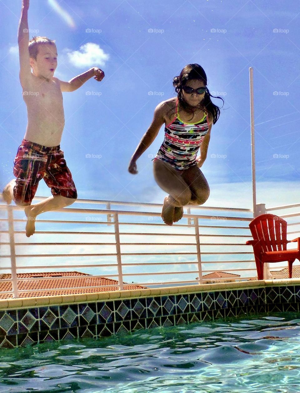 Siblings jumping into pool during summer vacation 