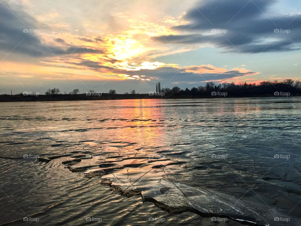 Frozen lake starting to defrost at sunset