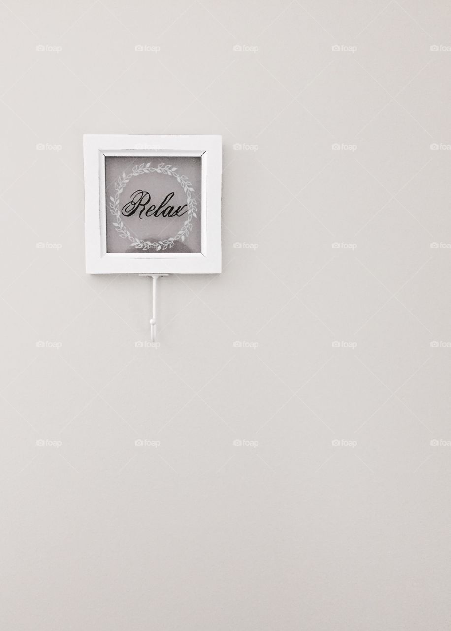 "Relax" - glass and wood plaque with hook and  the word "Relax" painted in black cursive lettering with a white laurel wreath around it on a neutral-colored wall