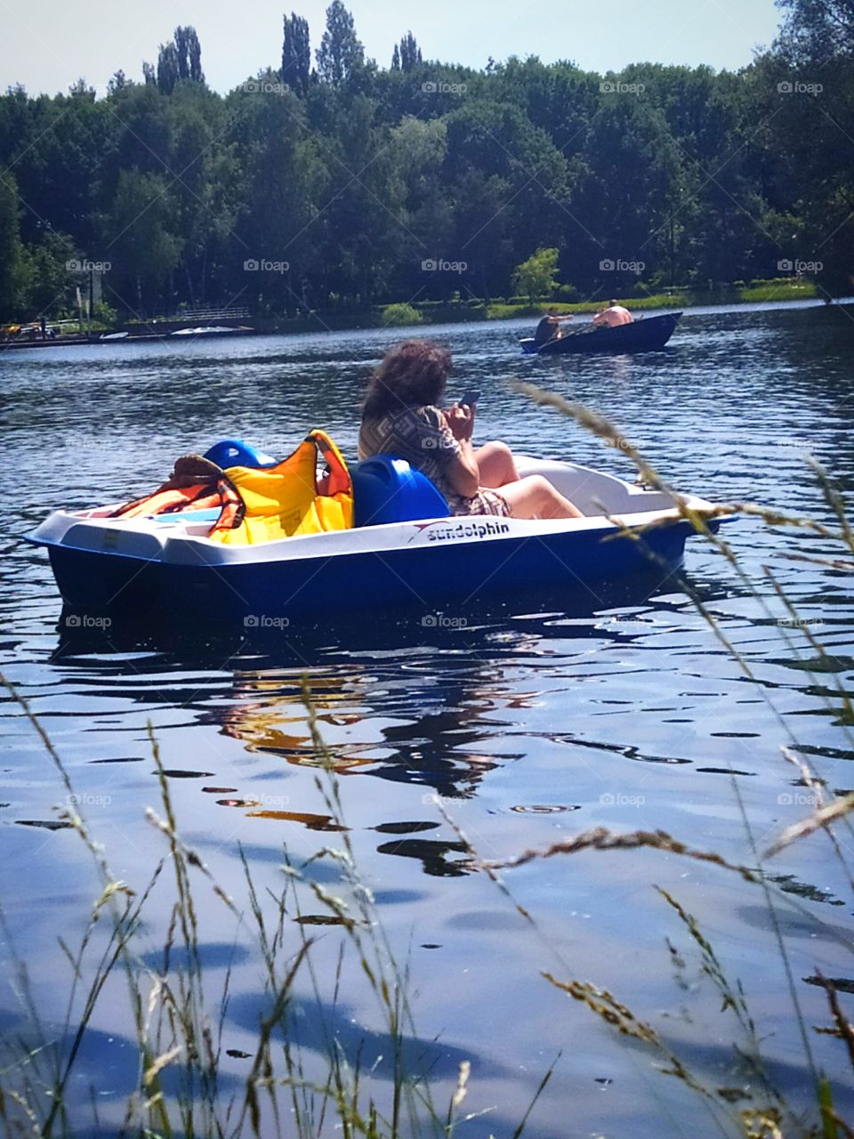 Summer.  Rest on the water.  A woman is sailing on a catamaran.  In the distance people are sailing into the boat