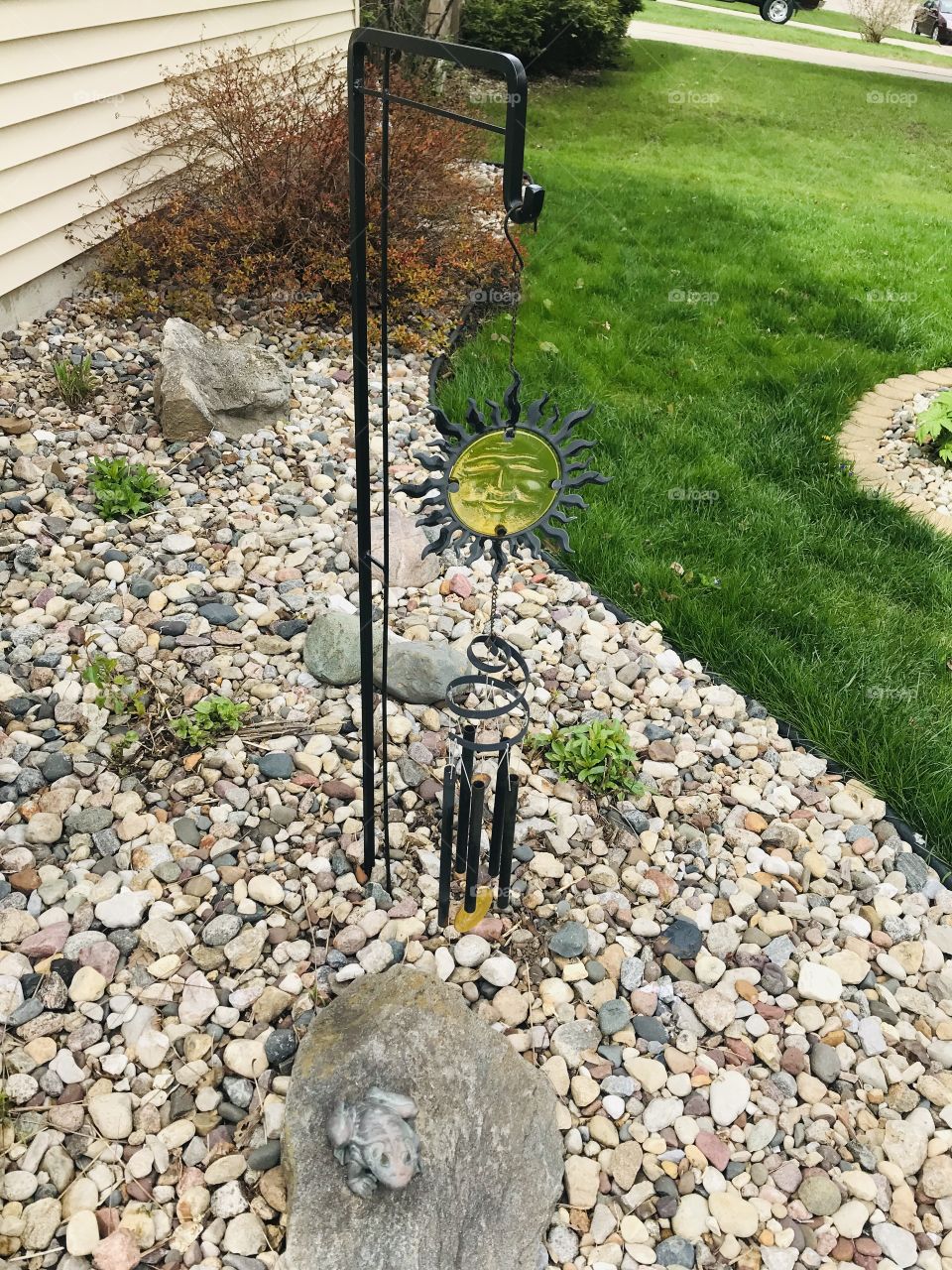 Gorgeous sun wind chime garden decor sitting against rock filled area background. 