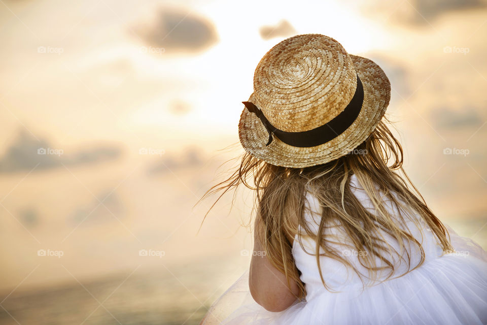 Little girl with blonde hair from behind looking on the sea on sunset 