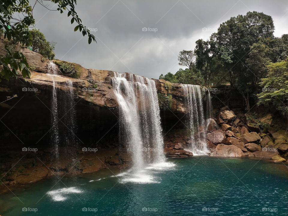 beautiful waterfall forming natural swimming pool surrounded by green trees captured in a cloudy day