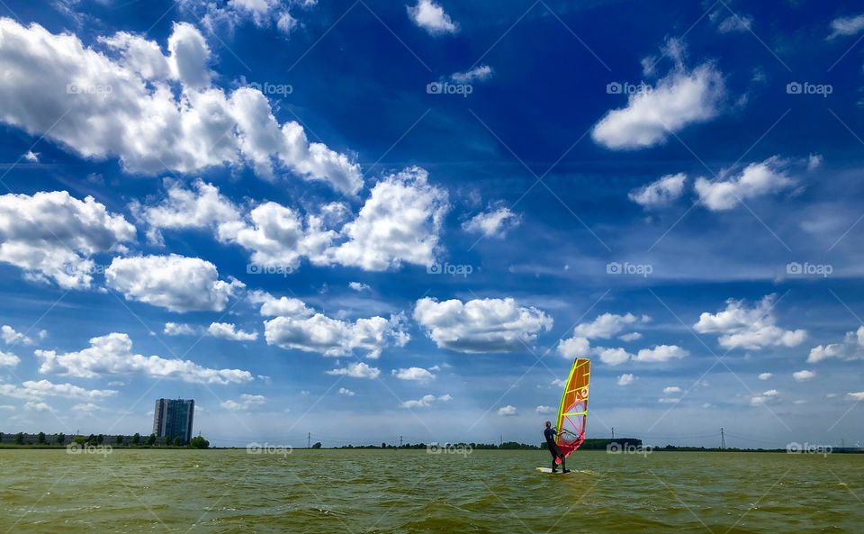 Windsurfers surfing the waves on a colorful surfboard against a city backdrop