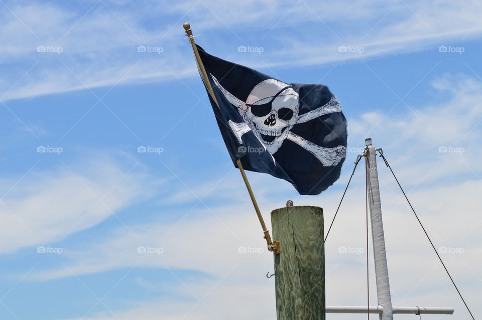 Skull and bones pirate flag flying in the air on ship mast