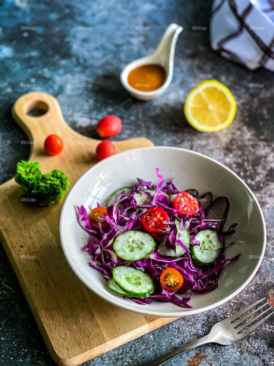 Fresh rainbow salad in a bowl, contains purple cabbage, cucumber, cherry tomatoes and some delicious sauce 