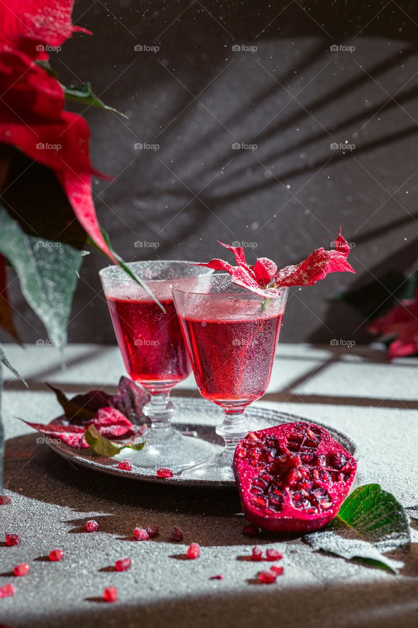 pomegranate cocktail is a refreshing bar drink. Winter stylization with poinsettia. The art of making and serving drinks, mixology. The play of light and shadow on the glass and background