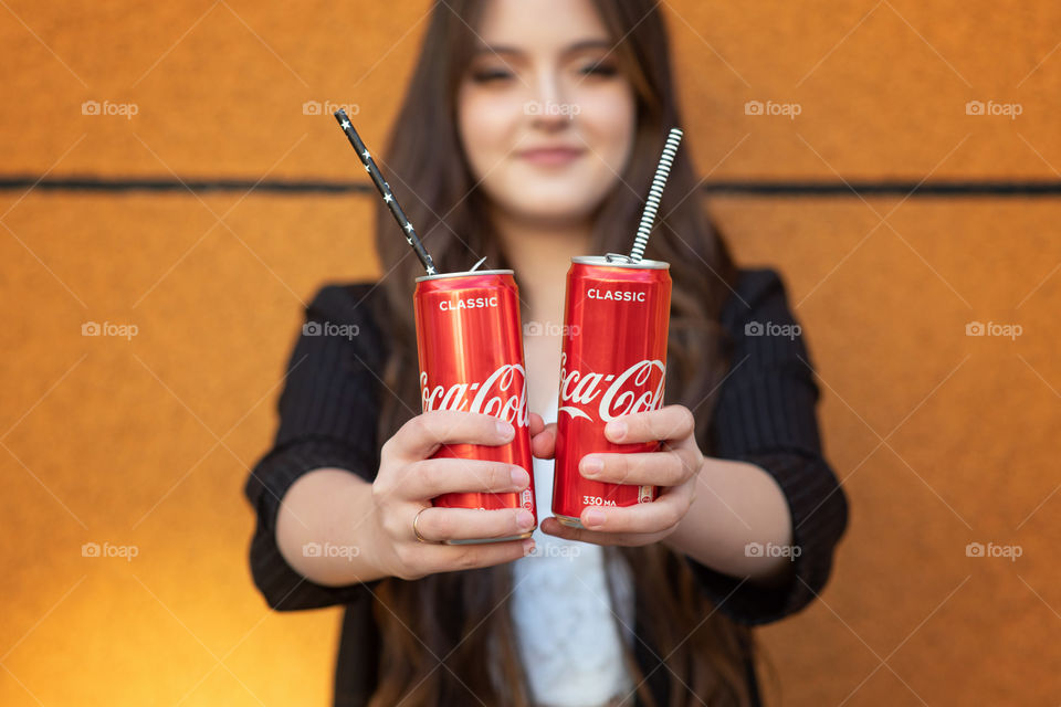 Young girl holds two cans of Coca-Cola with paper sticks inside