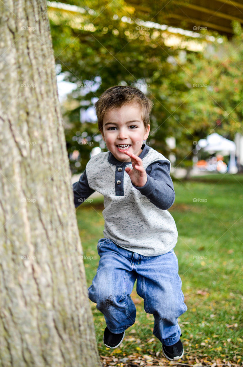 Young boy jumping behind a tree at the park