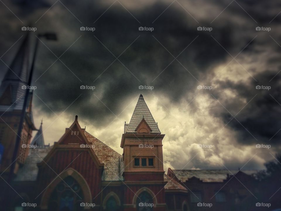 Storm clouds forming over a church with light coming in from the background.