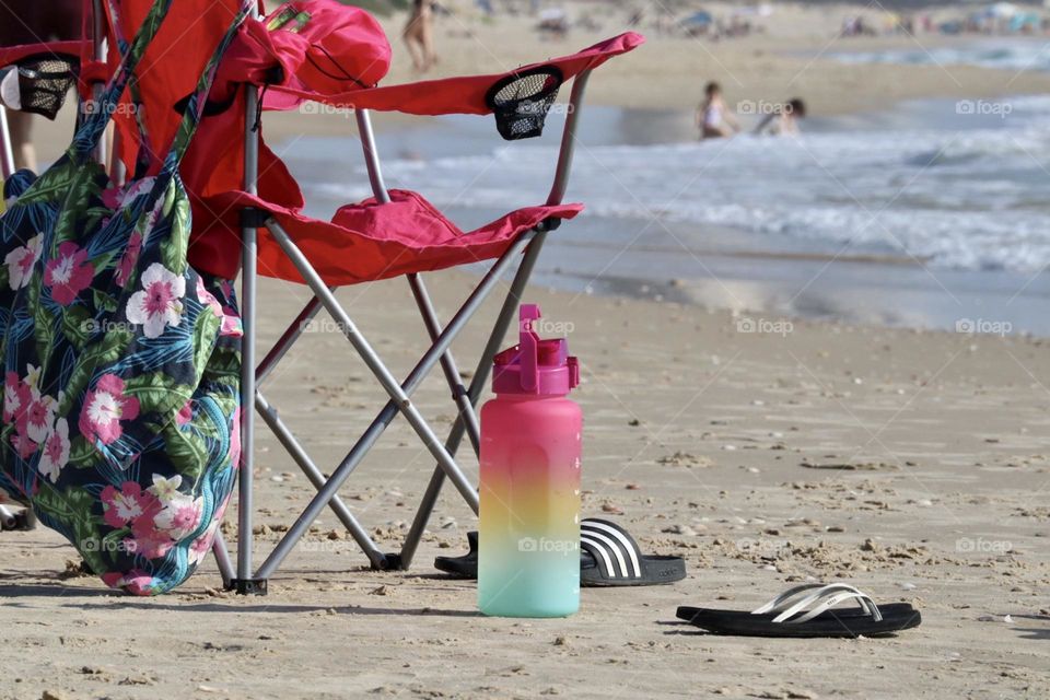 Colourful bottle near pink beach chair with flowers bag on the beach