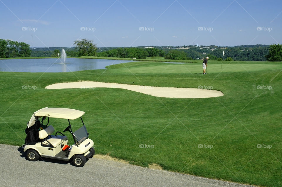 A man putting on the green, golf course, golf path and golf cart. 