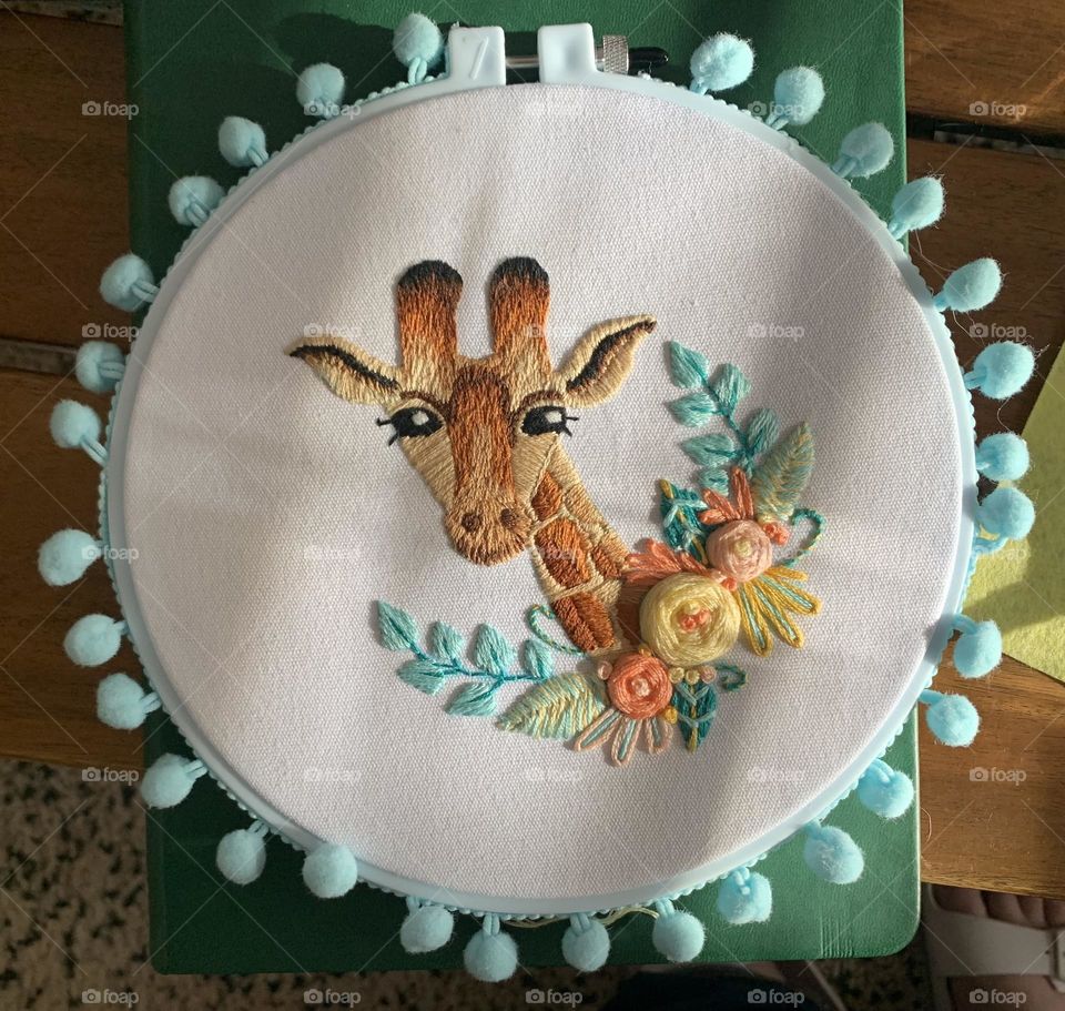Adorable hand embroidered giraffe with pastel floral accents. Created as a baby gift. Matching blue/green pom pom border. 