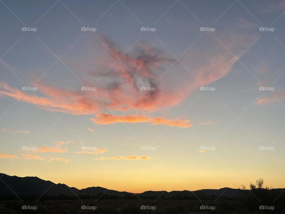 Pink and orange clouds above a beautiful sunset with mountains.