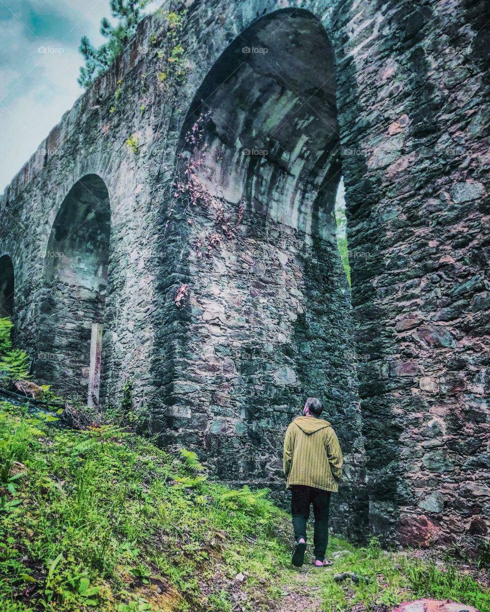 A man looks up at a old and unused stone aqueduct that towers over him