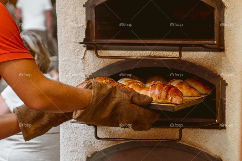 The baker pulls out appetizing rolls from the oven.