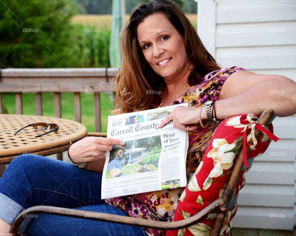 Woman sitting on chair with newspaper at patio