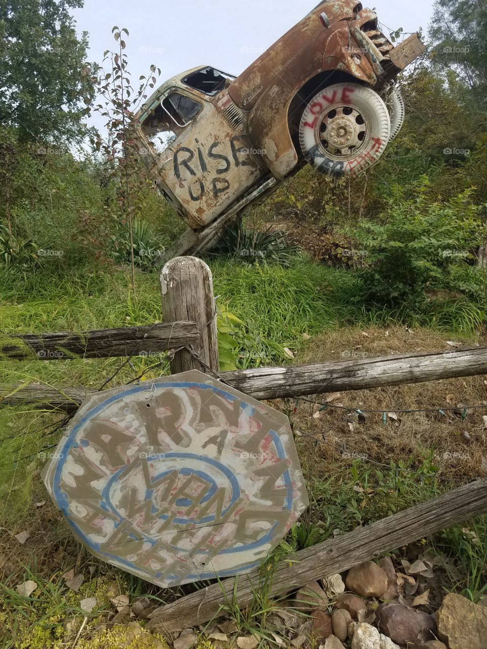 Erected truck at truckhenge that reads "RISE UP". Below is a sign saying "WARNIMG S MAN WITH IDEAS".
