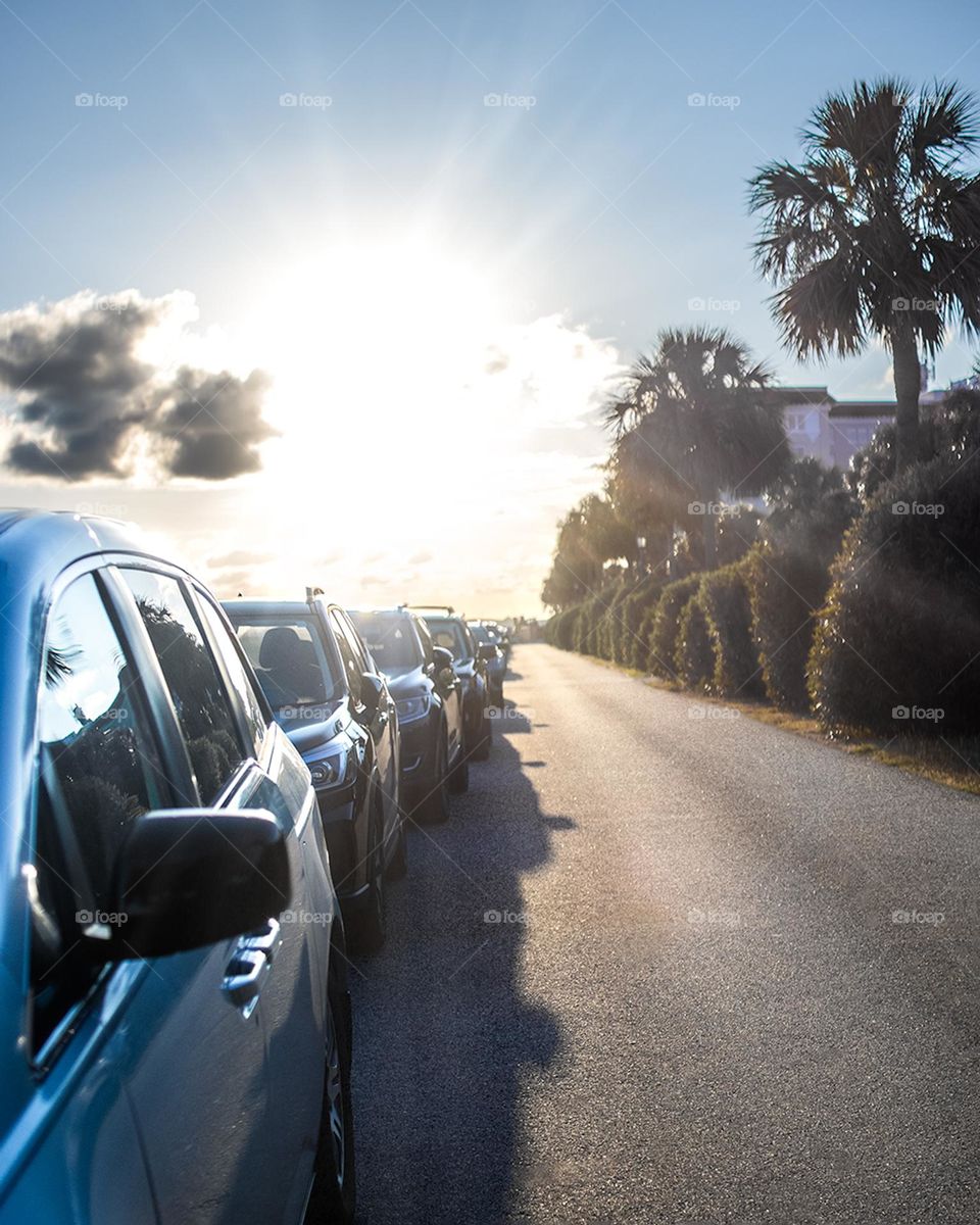 Sunset near the beach with cars parked nearby. 