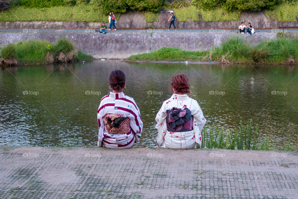 In Kyoto, old and new Japanese culture mesh seamlessly. Two friends in traditional kimonos take in the calm beauty of the Kamo River after a peaceful evening stroll. 