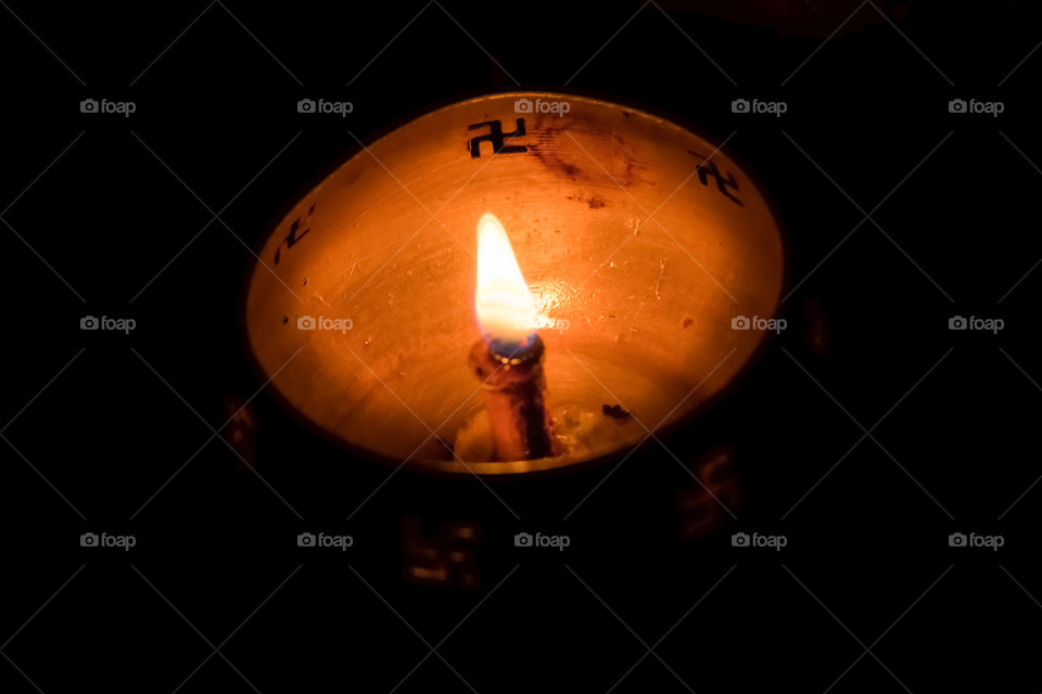 A traditional handicraft candelabrum vintage old and rustic bronze metallic Buddhist oil lamp spreading light against art dark background.