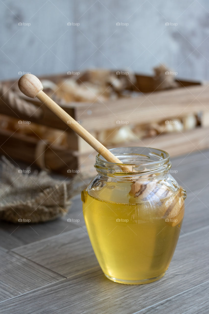 Honey in glass jar with wooden spoon on the table at rustic blurred background.