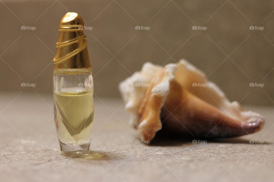 Small bottle of light golden perfume with shell shaped cap next to a seashell on granite counter