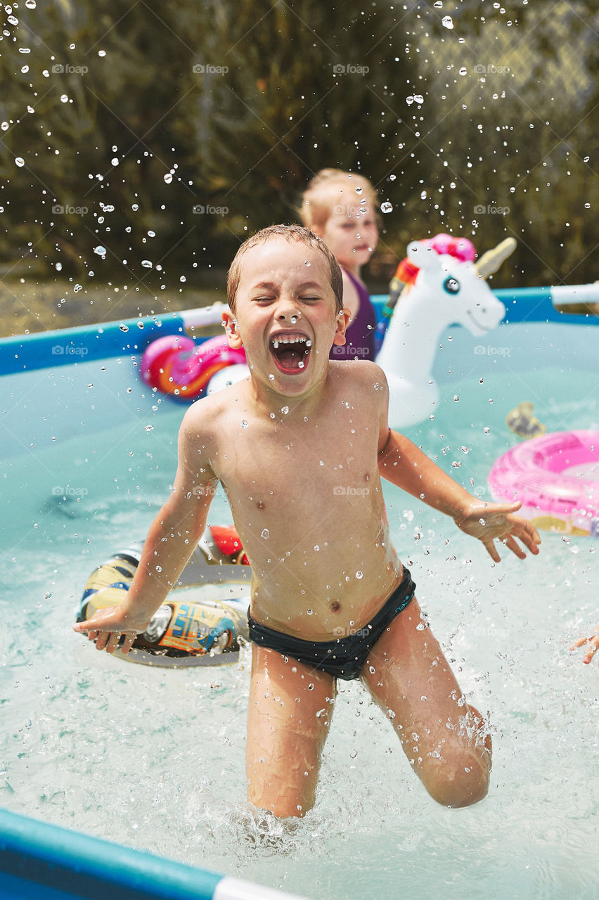 Boy jumping in a pool enjoying splashing having fun with siblings on a summer sunny day