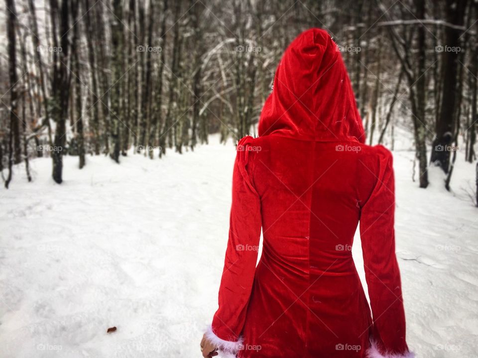 Back of woman wearing red coat with red hood in a forest of snowy trees