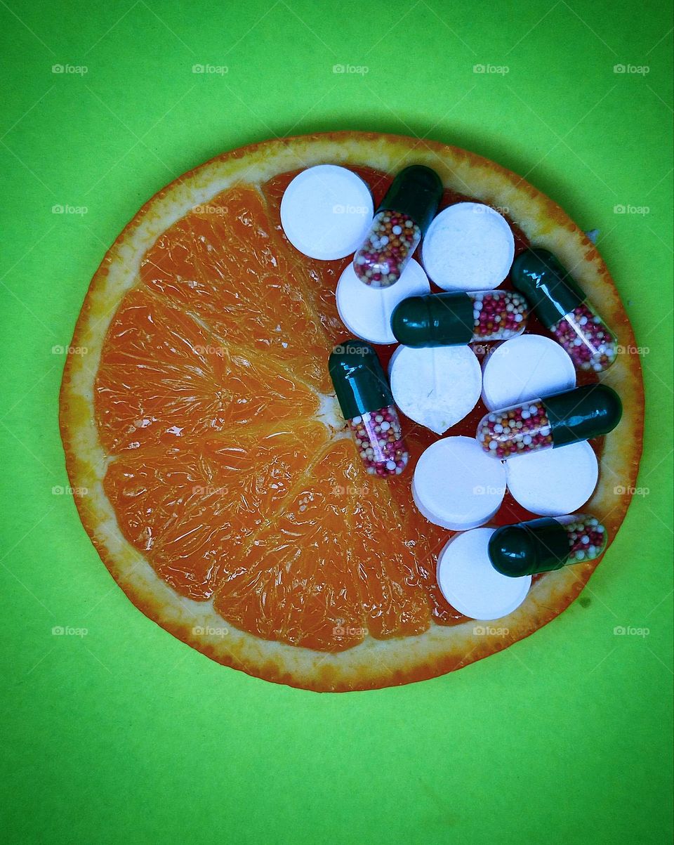 Healthy diet.  Vitamins natural and in medicinal forms.  On a green background lies a cut orange, half of which is filled with vitamins in capsules and white tablets.  Selection for natural fruit