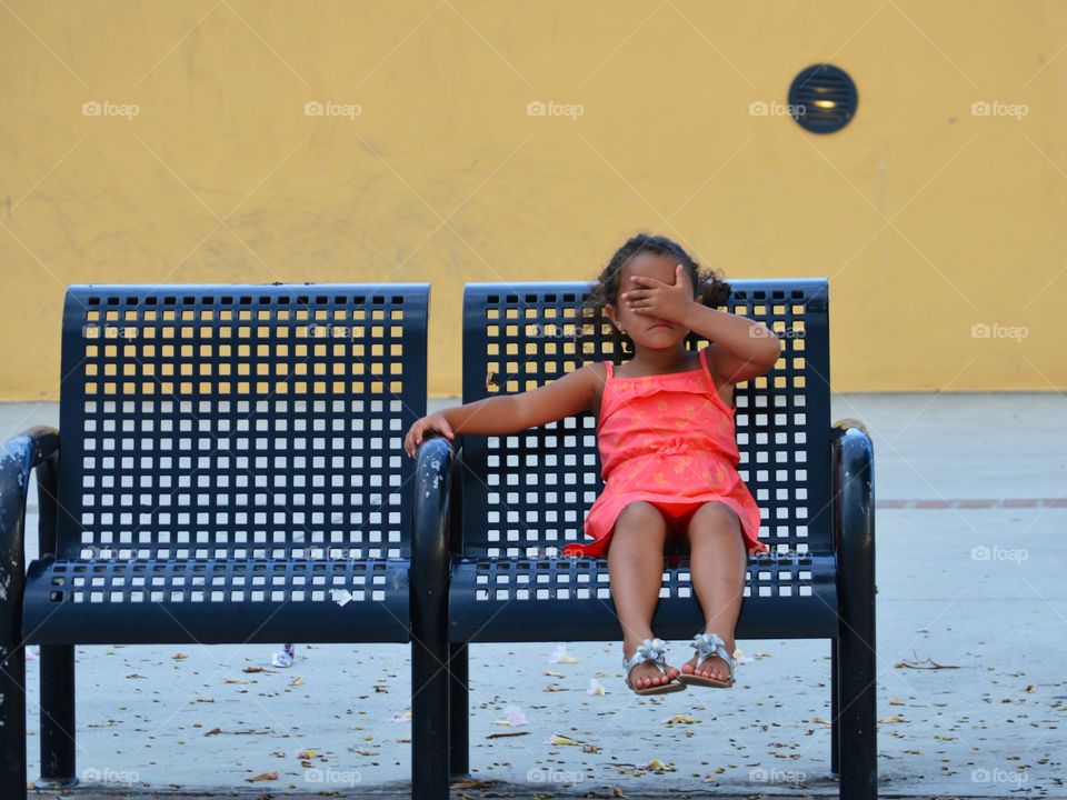 You can't see me. tired little girl sitting on a bench