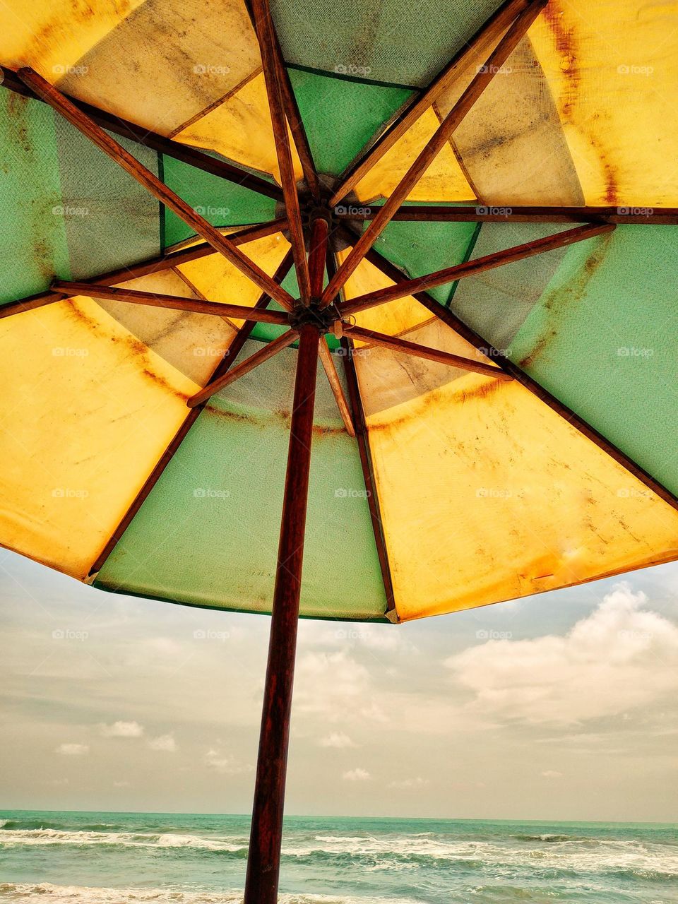 A green and yellow parasol, waiting for someone to have fun on the beach and rest in its shade.