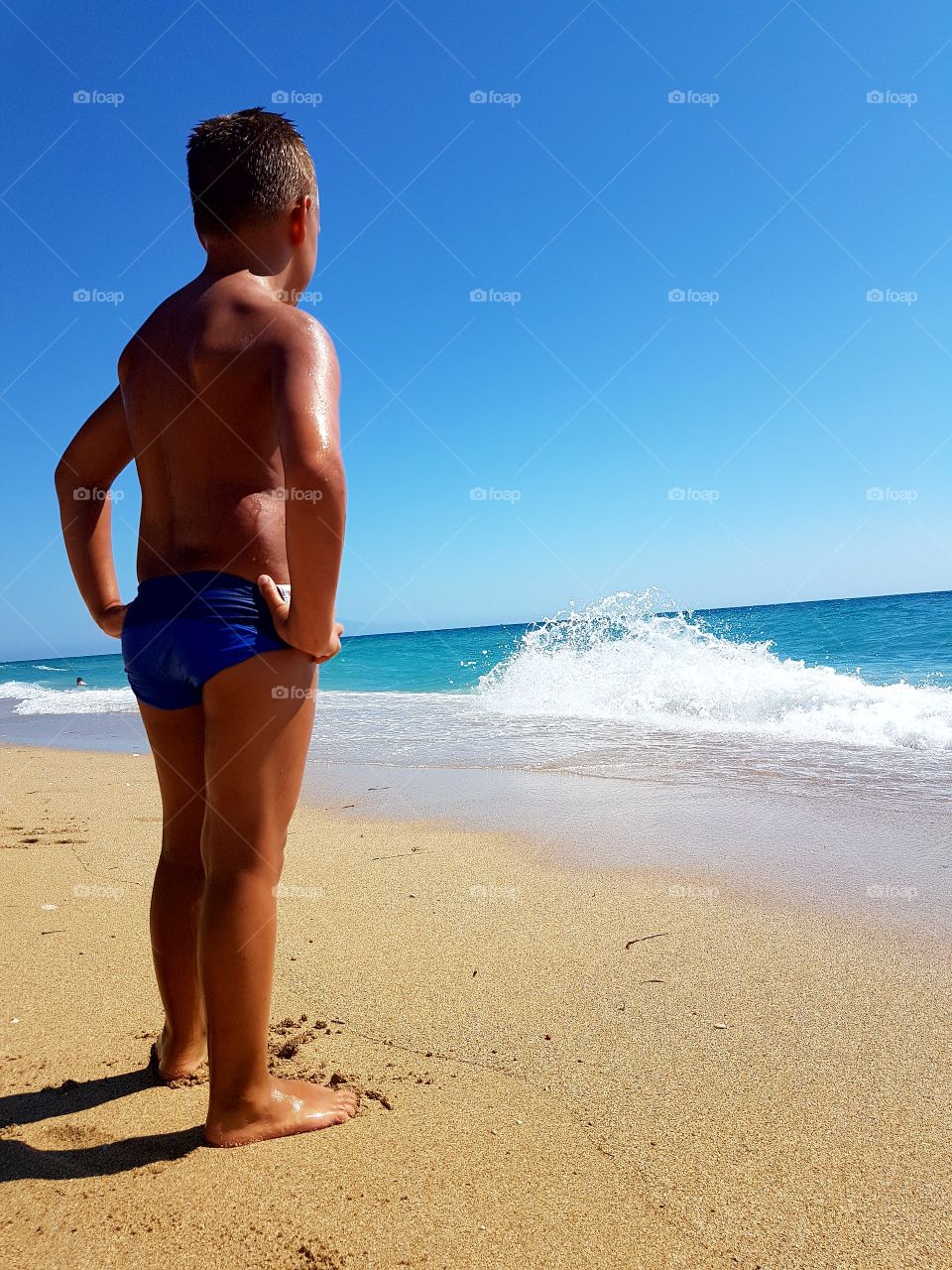 Boy standing on the beach looking at the waves