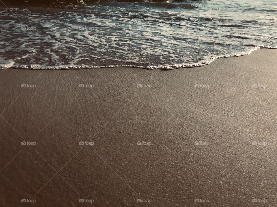 Surface level view of late afternoon sunlight on smooth sand at shoreline 