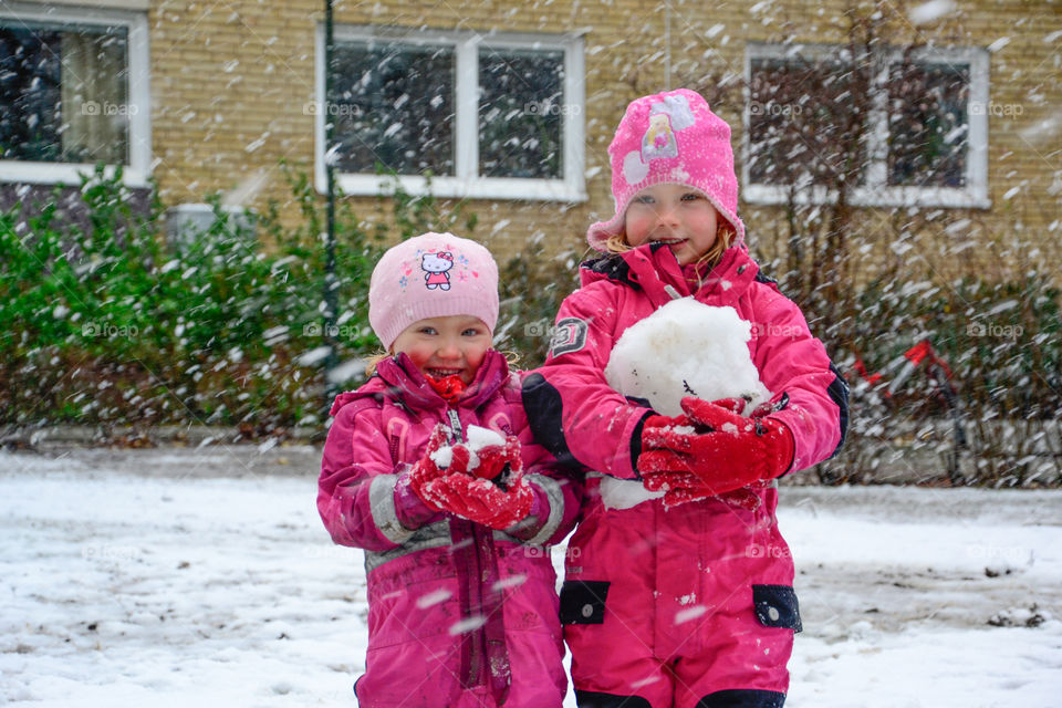 Two young sisters is playing in the snow.