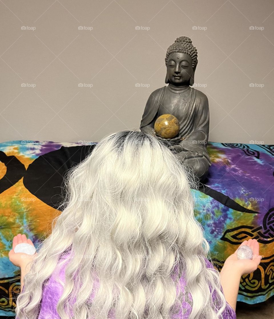 A woman meditating with a Buddha statue.