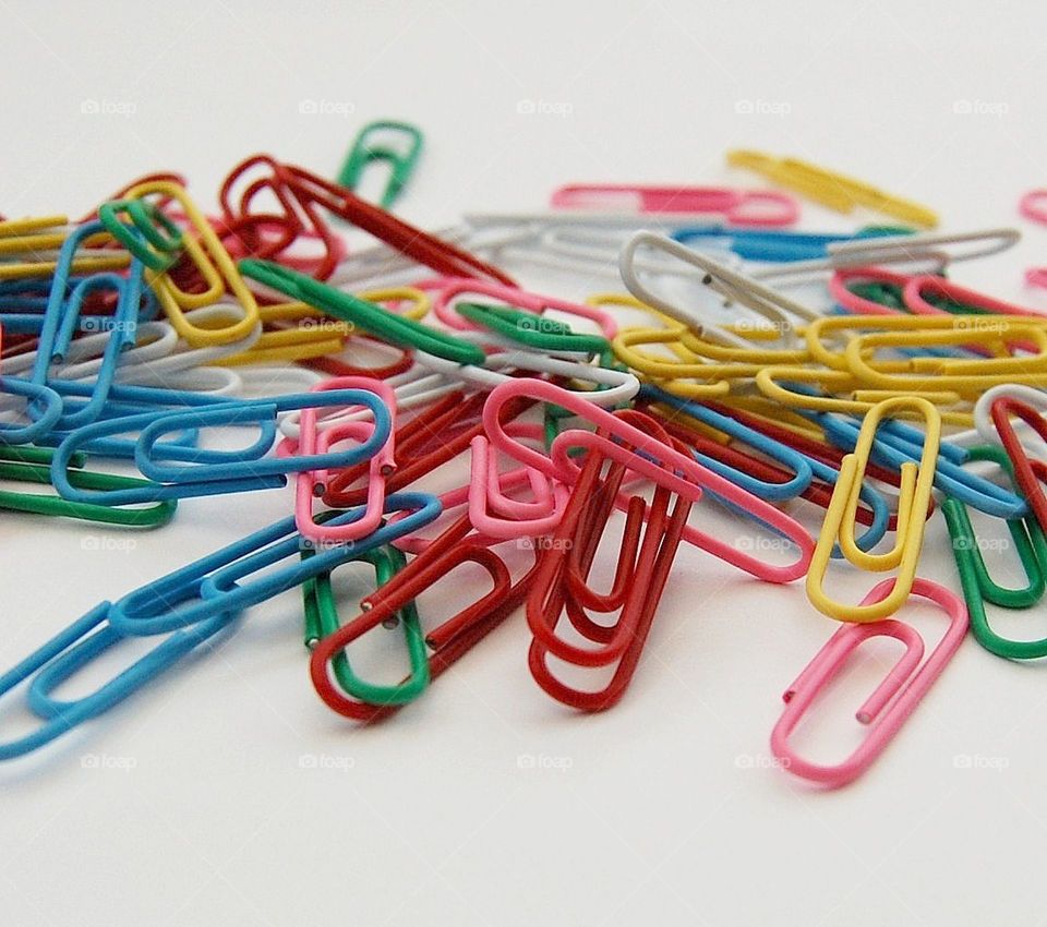 Scattered paper clips in various colours in a pile against a white plain background 