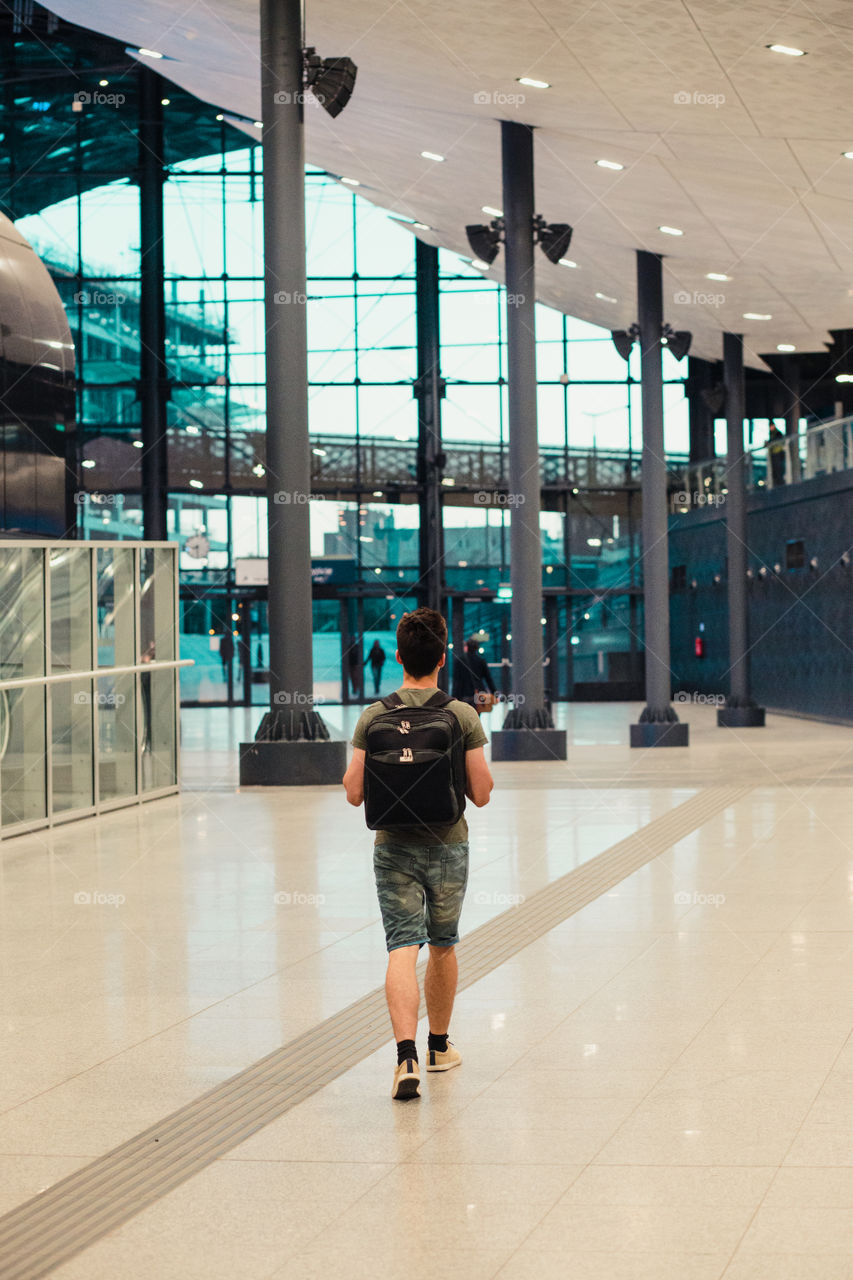 Young man walking in the railway station, travelling with backpack