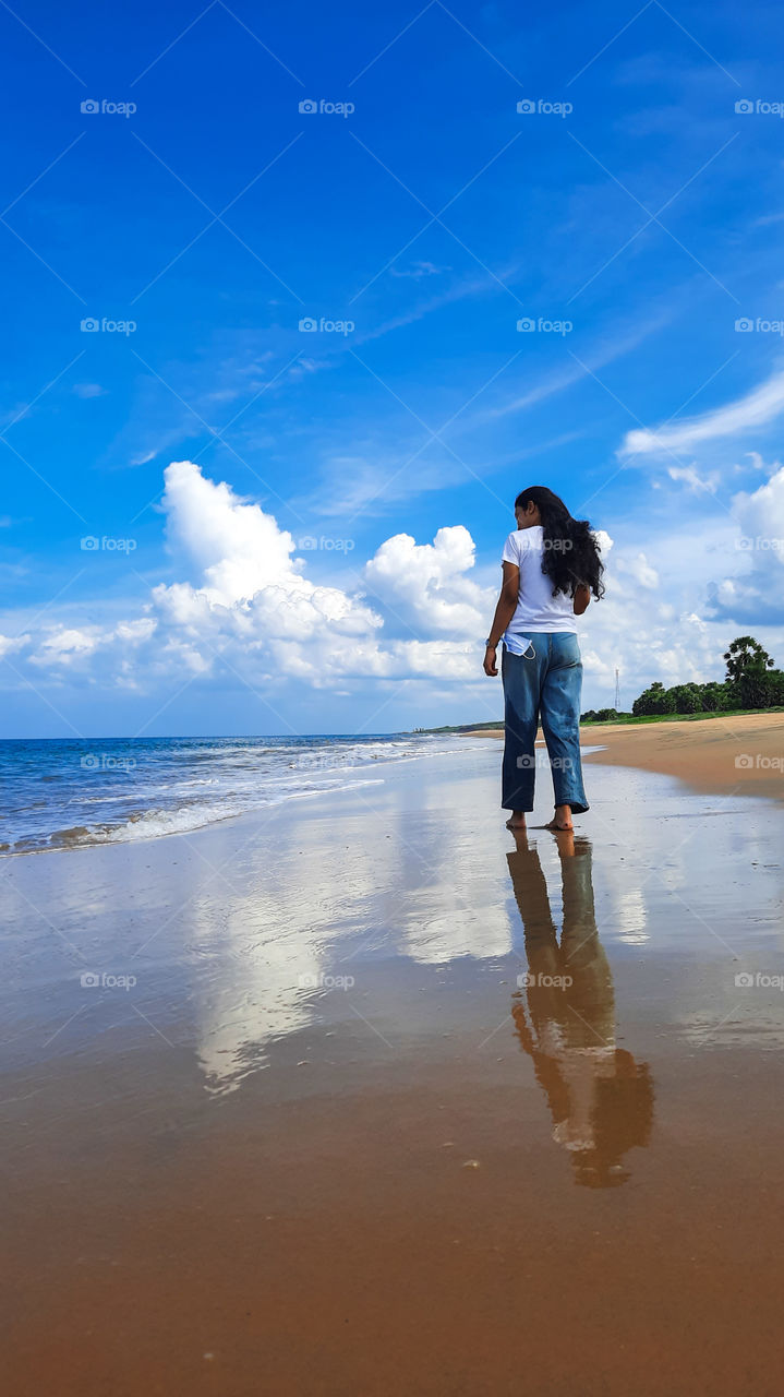 Walk along a magical beach surrounded by beautiful blue ocean, nice sunny sky with clouds, white smooth waves and golden sandy beach with water reflects what you are.