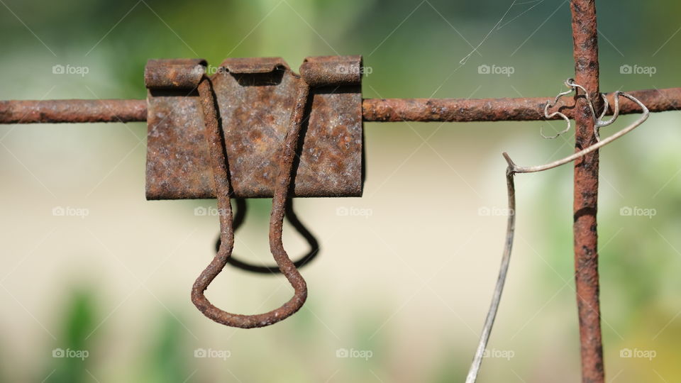 Rusted metal paper clamp hanging from a wire fence.