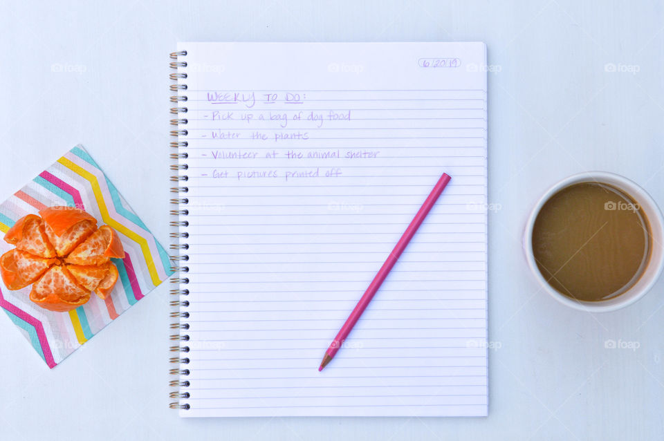 Flat lay of an open notebook with a written to do list, an orange, cup of coffee and pencil
