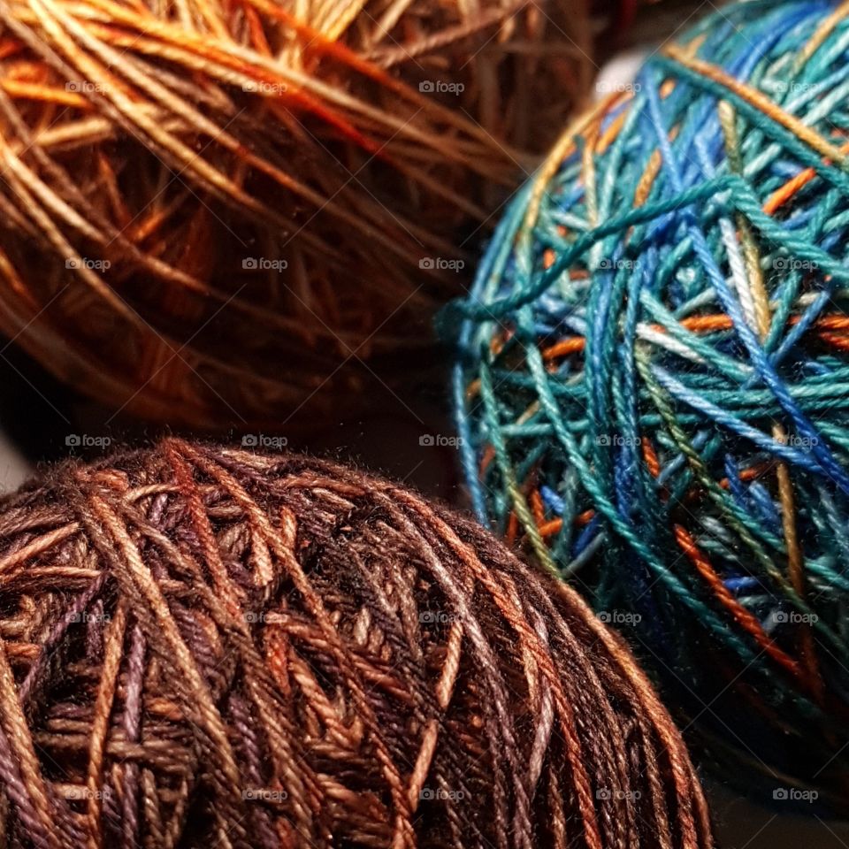 Three balls of yarn in orange, brown, and teal