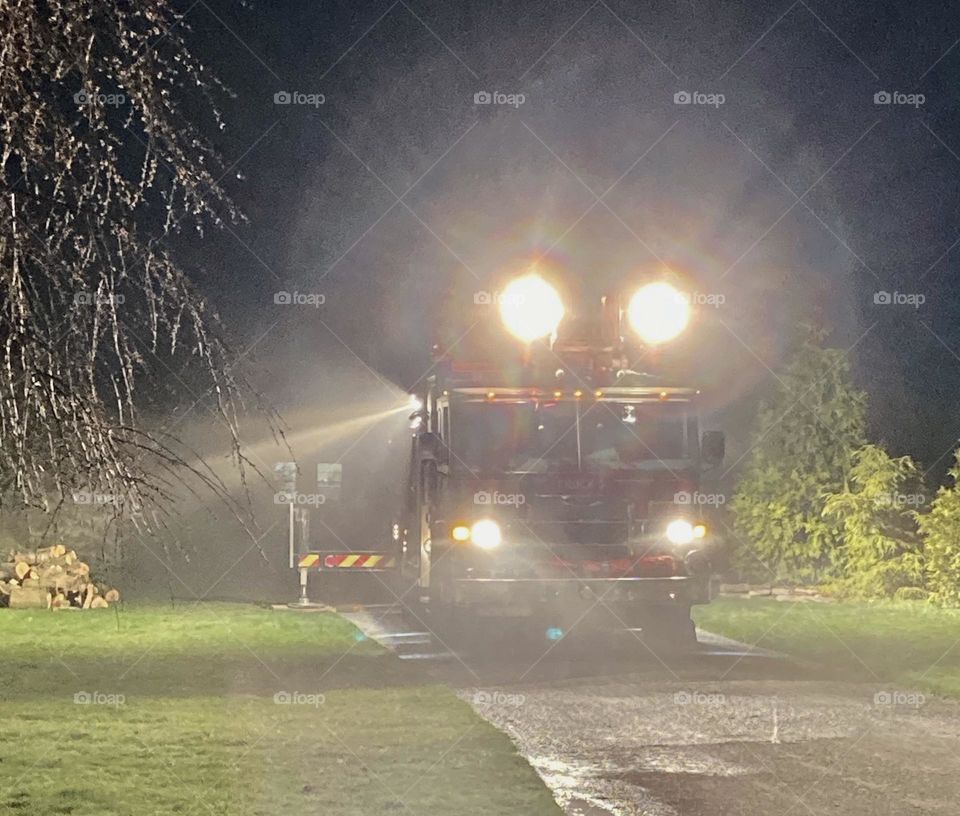 A fire ladder truck working a house fire at night with auxiliary lighting, piercing the smoky air