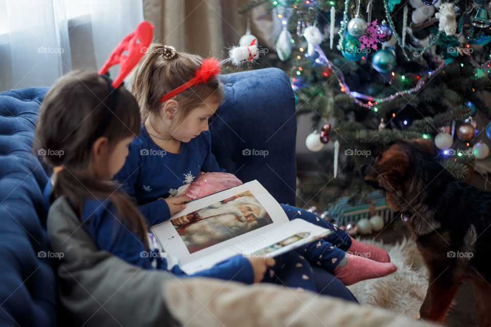 Little sisters reading a book at Christmas time 