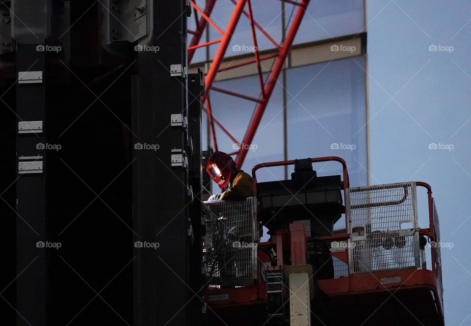A welder works on a new high rise under construction in New York City and the arc flash is reflected in his face shield