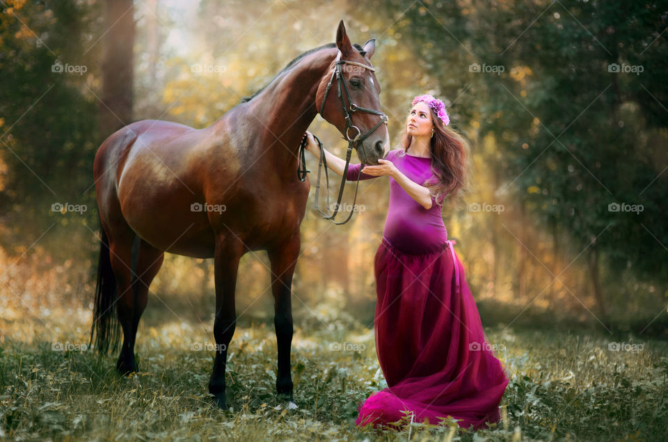 Young pregnant woman with horse in sunny forest