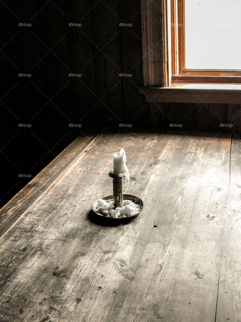 A candle on an old wooden table by a window