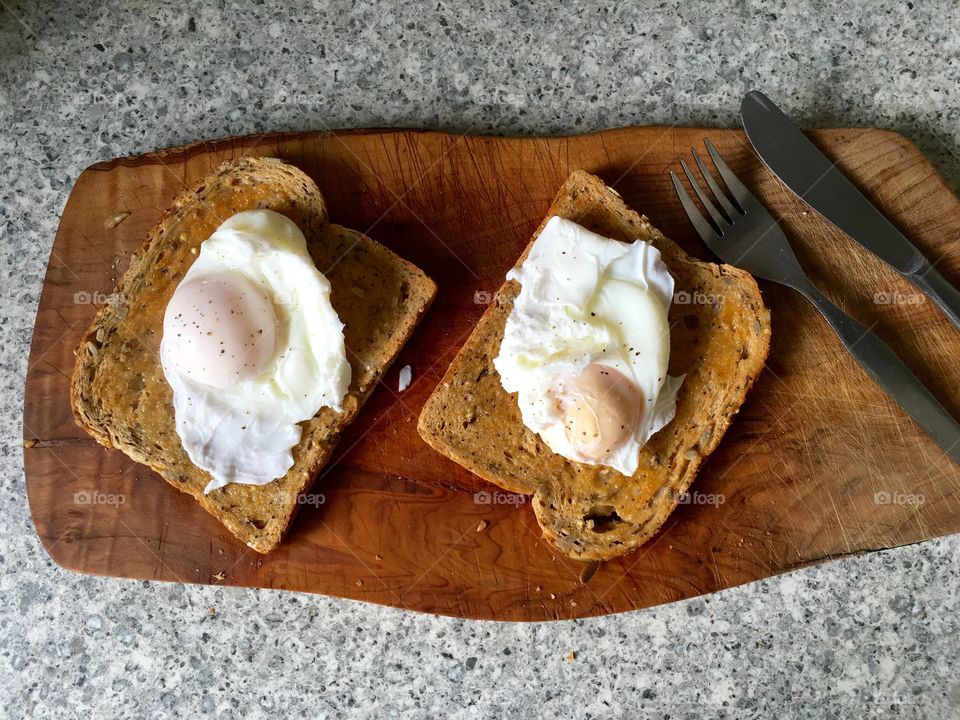 Poached eggs on toast on olive wood with cutlery 