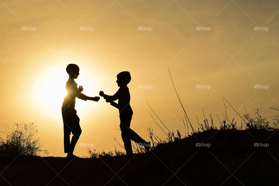 silhouette of two child playing against dramatic golden hours sky