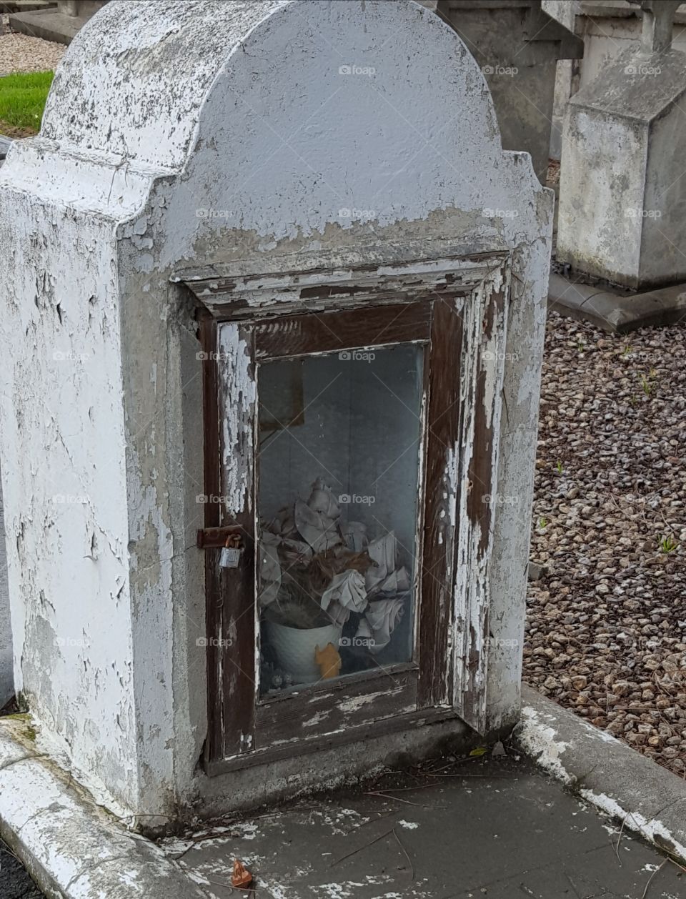 a very old gravesite where the tombstone is more of a niche to place offerings, light candles or bouquets of flowers. the rusted lock shows it has been sometime anyone has opened it.